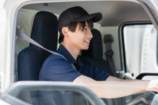 トラックの運転席で笑顔を見せ、安全にハンドルを握る男性ドライバー