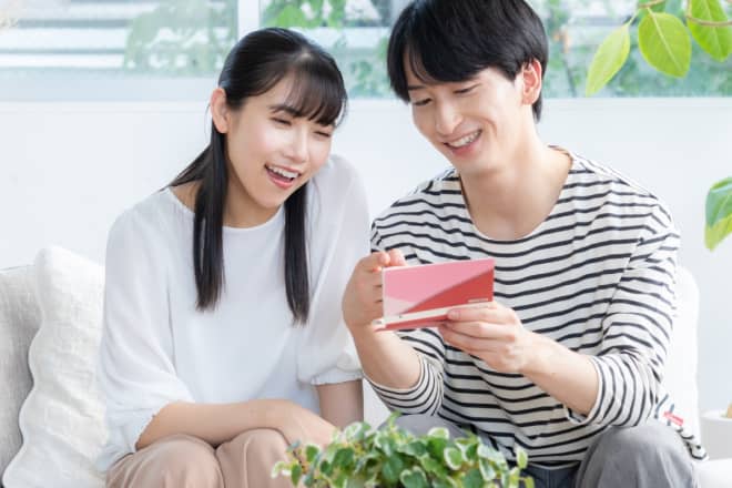 リビングで仲良く通帳を眺め、笑顔で話し合う若い男女