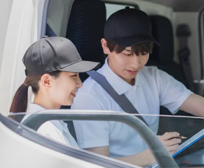 トラックの運転席で指示書を確認する男女の配送スタッフ。