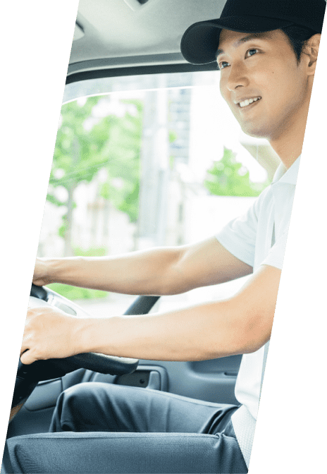 トラックの運転席で笑顔を見せながらハンドルを握る、黒いキャップを被った男性ドライバー